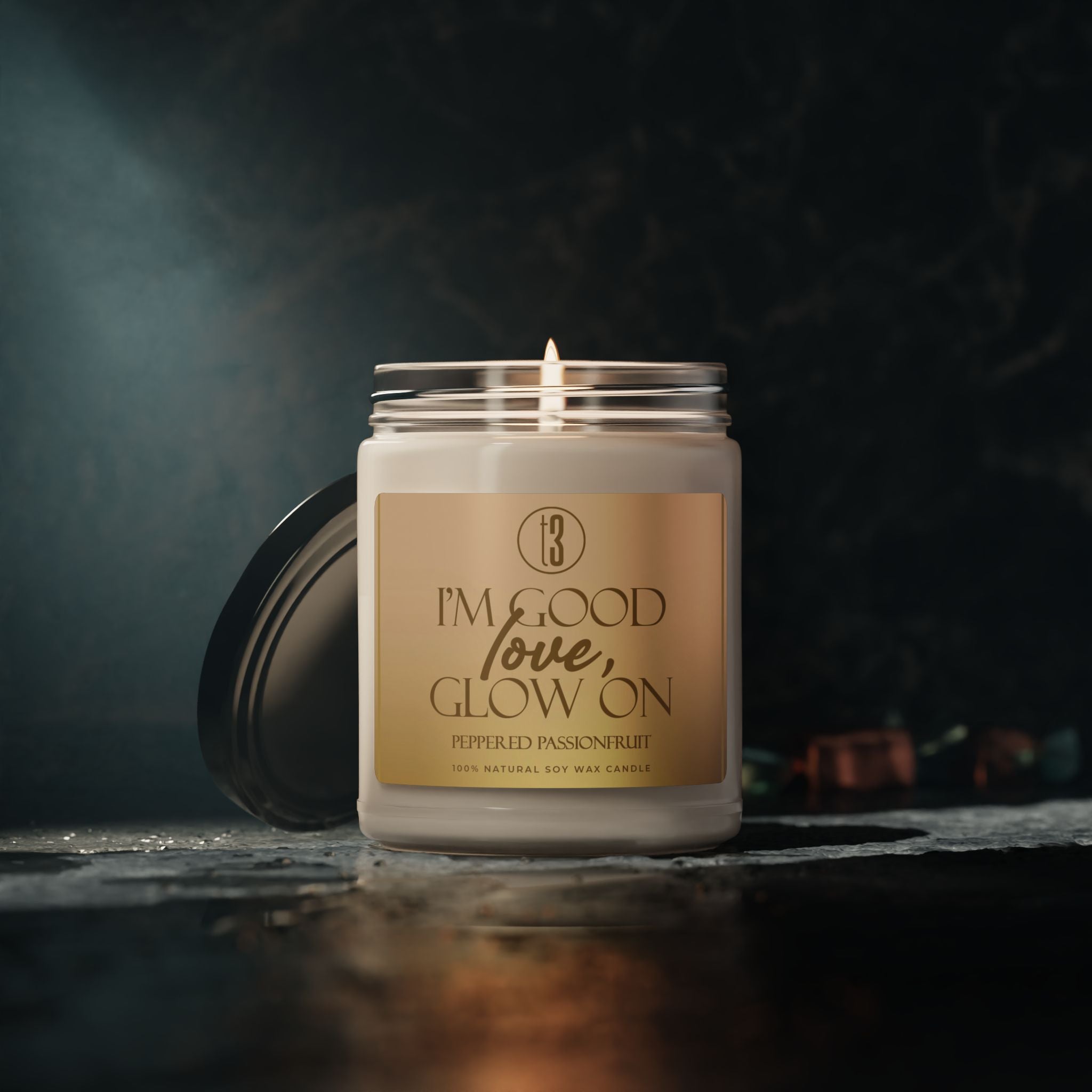 “I’m Good, Love, Glow On” aromatherapy candle from T3 Wellness, shown in three views: lit with a moody background, and unlit with lid on and off. Housed in a glass jar with a beige label and black text, this hand-poured candle features a citrus-forward fragrance blend of juicy orange, melon, pineapple, jasmine, and passionfruit. Designed for emotional grounding, relaxation, and self-care rituals. Available now at teatimewithtoniya.com.